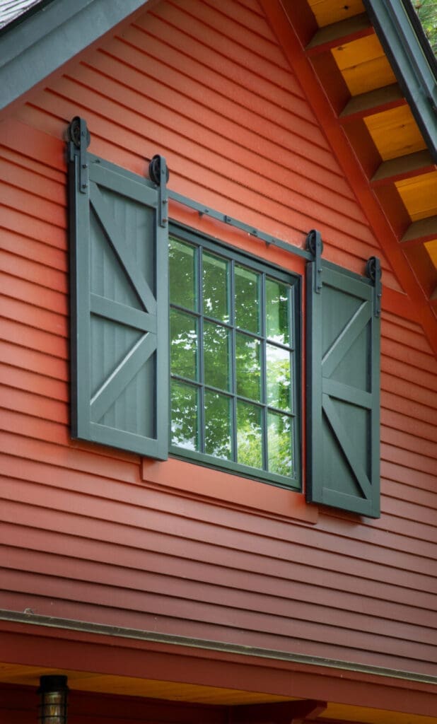 A photo of a barn-style forest green window on the front of a red garage.
