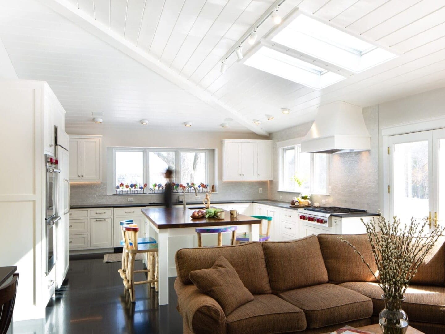 A photo of a kitchen with shaker-style cabinetry, silver hardware, a black stone countertop, stainless steel appliances, an island with a natural wood top, skylights and recessed lighting.