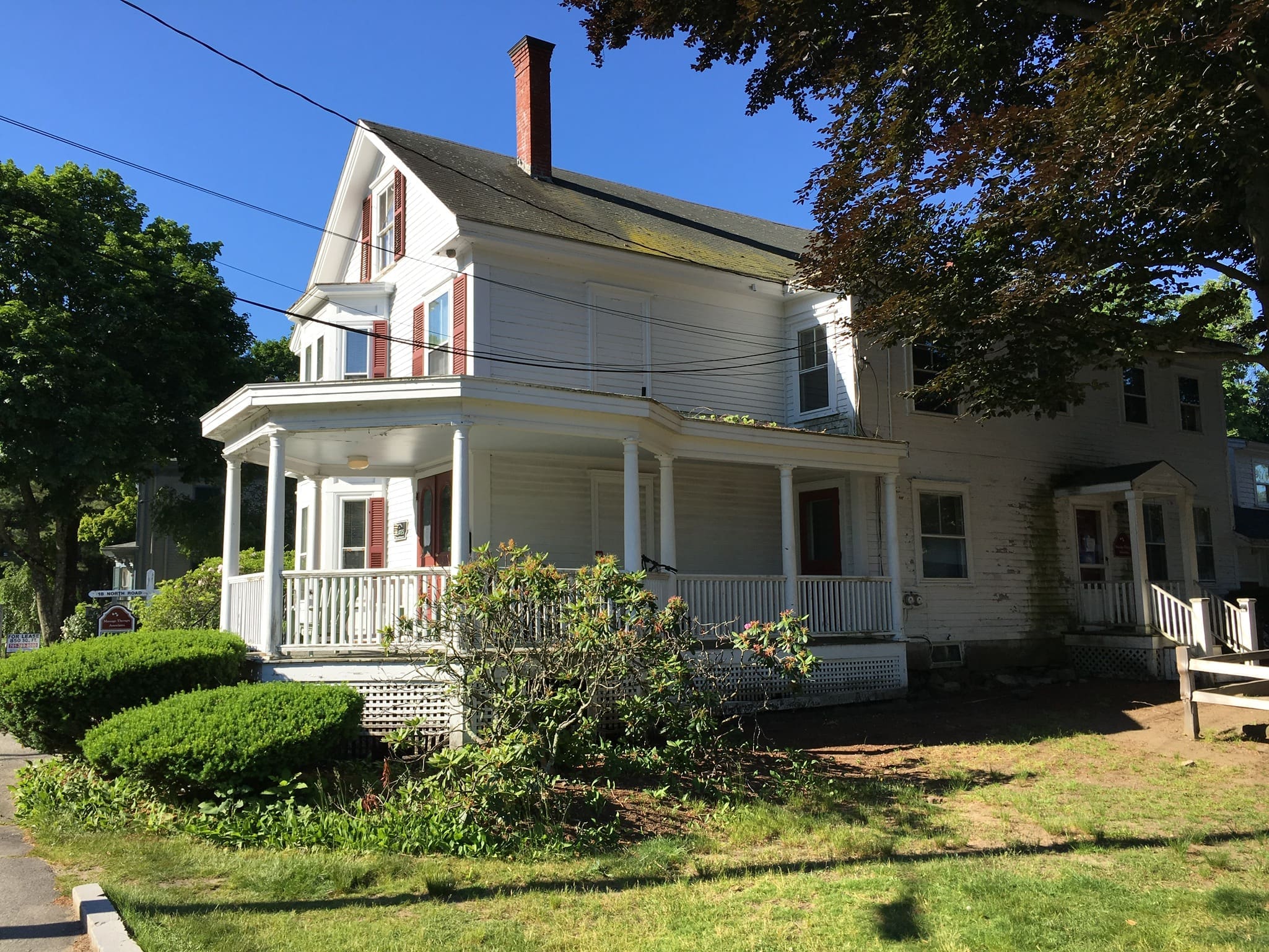 A white house with a porch and bushes in front of it.