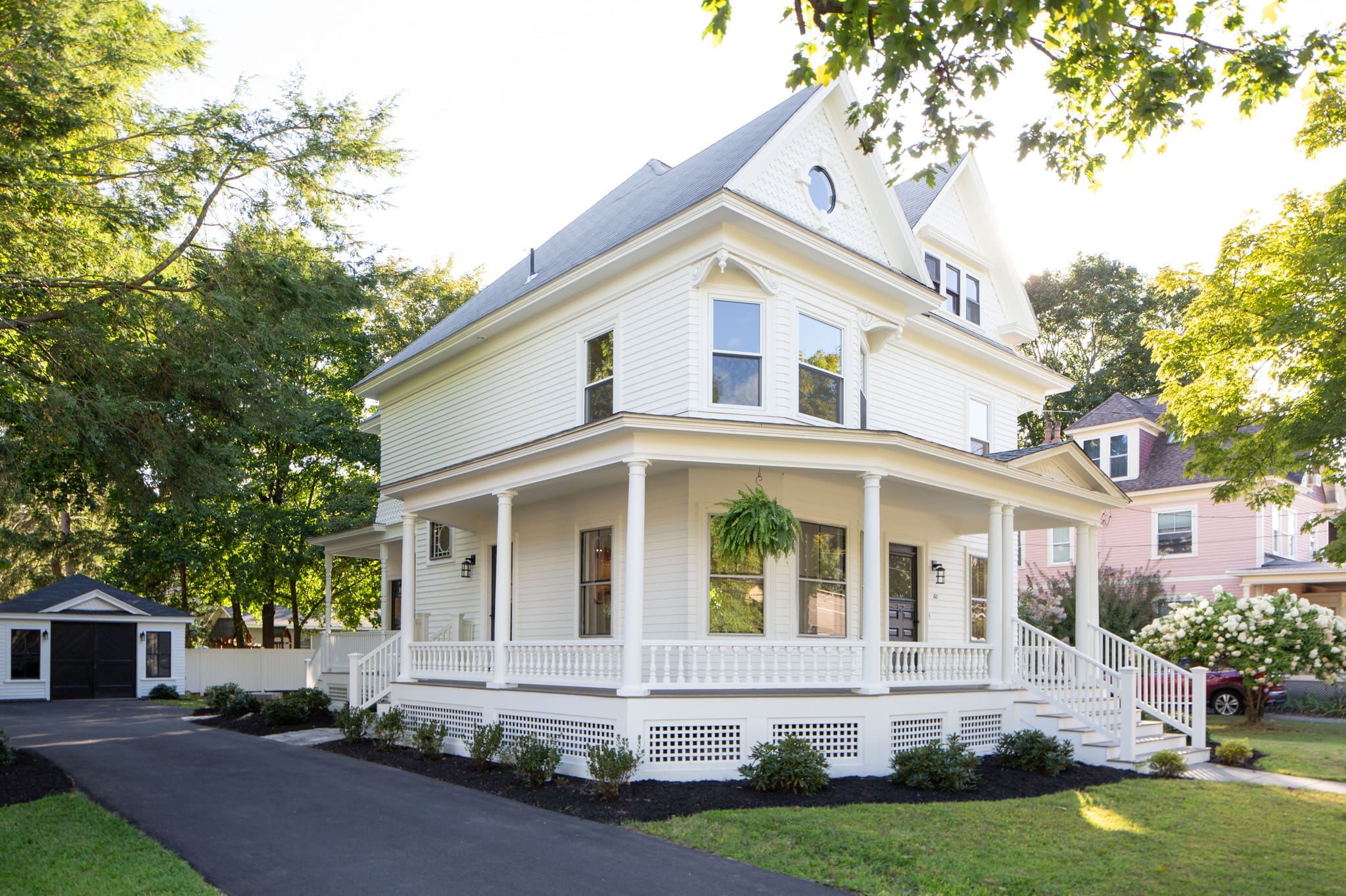 A large white house with a porch and green plants.