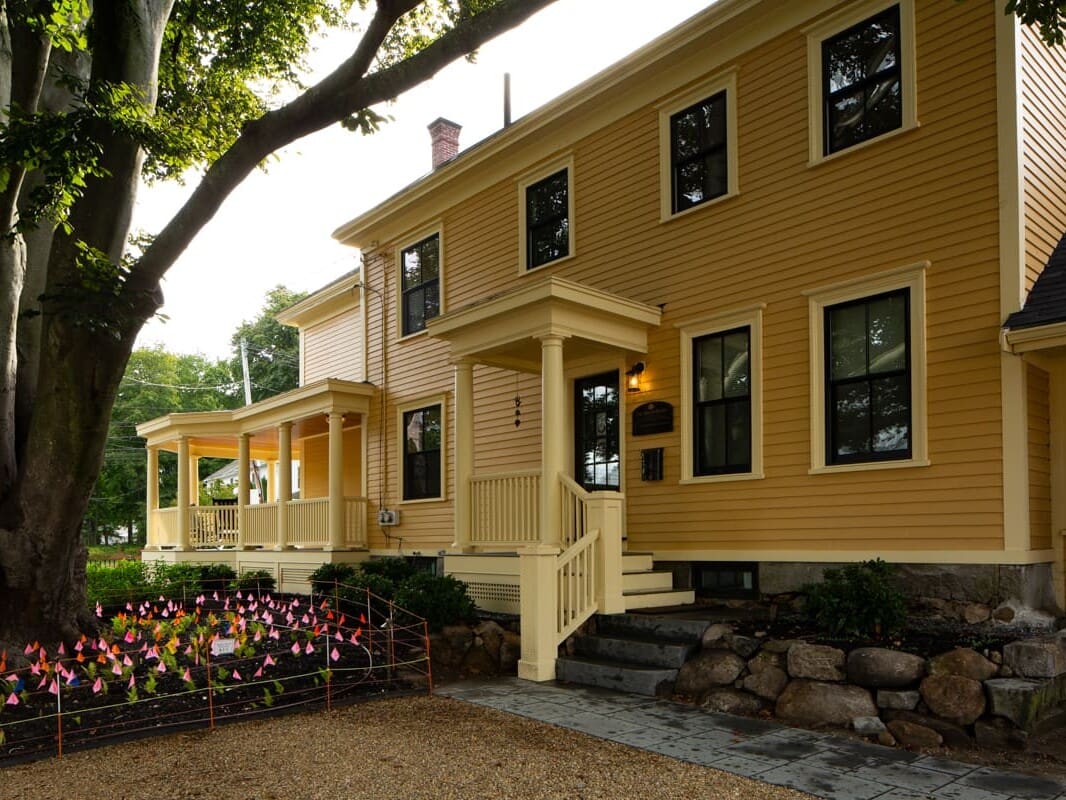 A yellow house with flowers in front of it.